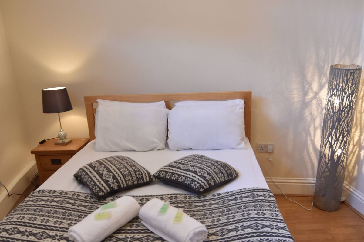 A neatly made bed with patterned bedding, a bedside lamp, and a tall, decorative floor lamp.