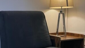 A dark-colored sofa positioned against a wall, with a floor lamp with a beige shade and a wooden base to the right. - Brighter Properties (London)