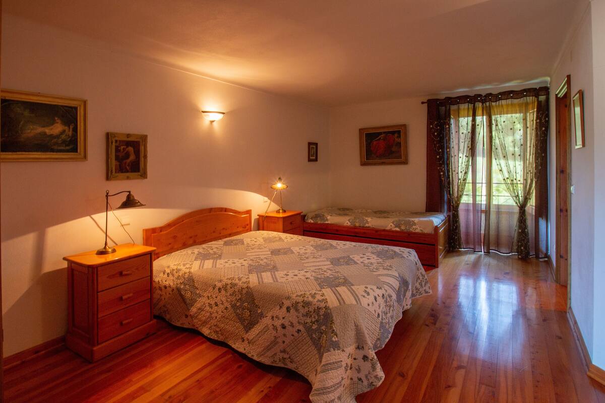 A bedroom with two beds, wooden flooring, and wall-mounted lamps.