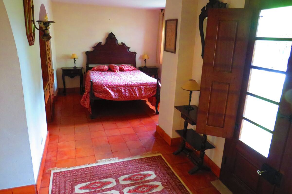 A bedroom with a wooden bed, two bedside tables with lamps, a wooden wardrobe, and a large window.