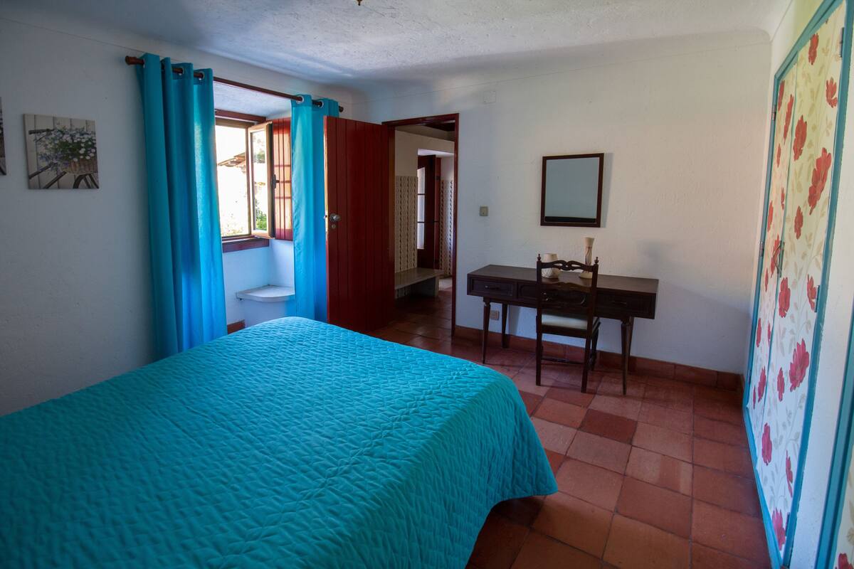 A bedroom with a bed, a desk, and a bathroom visible through an open door.