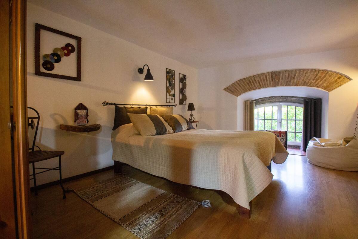 A bedroom with a bed, a chair, a lamp, and a window with a view.