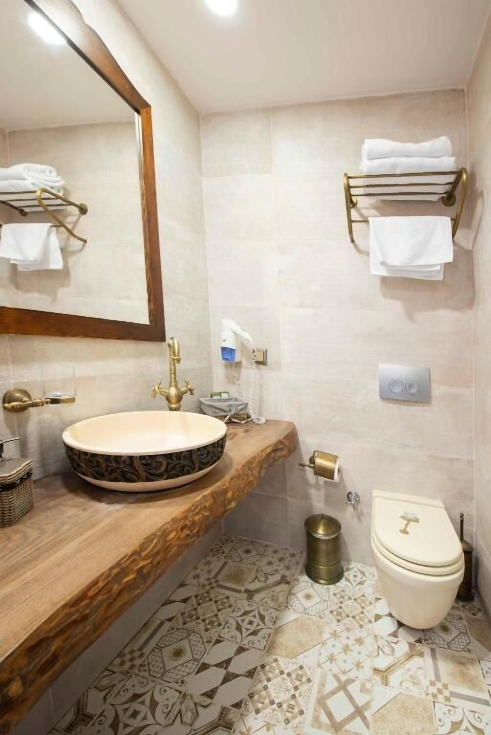 A bathroom with a round sink, a toilet, a mirror, and towel racks.