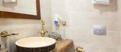 A bathroom with a round sink, a toilet, a mirror, and towel racks.