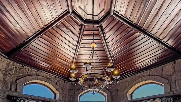 Um quarto amplo com uma cama grande, um lustre, paredes de pedra e janelas grandes.