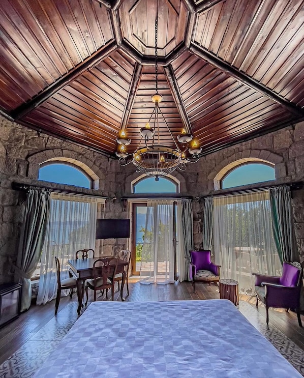 A spacious room with a large bed, a chandelier, stone walls, and large windows.