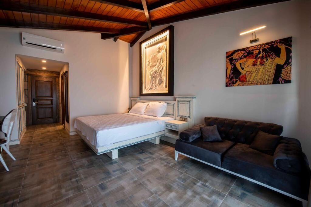 Un dormitorio con cama, mesita de noche, sofá, un cuadro y techo de madera.