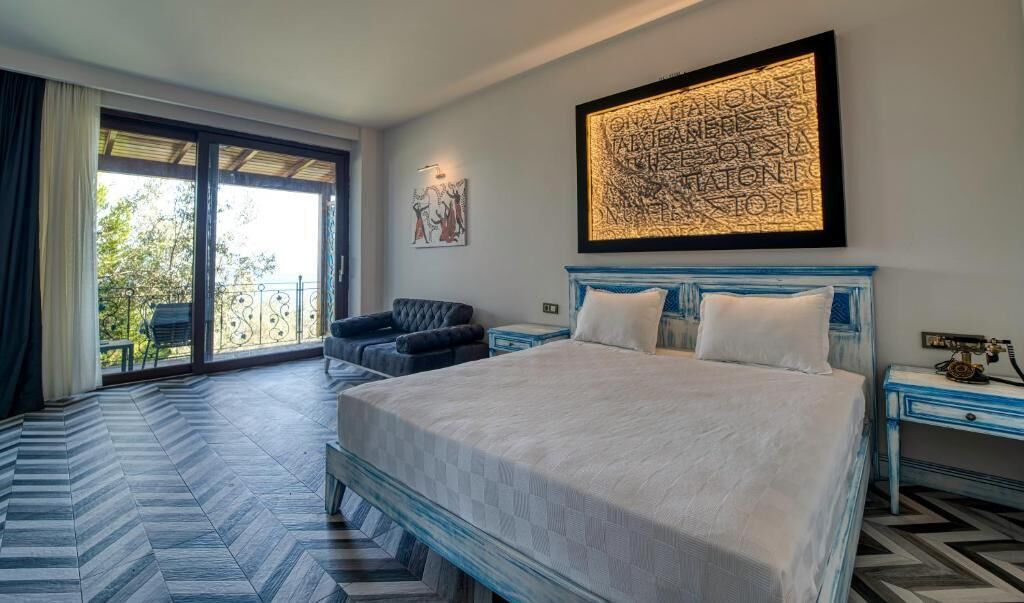 A bedroom with a large bed, a chair, a nightstand, and a large window with a view of trees.