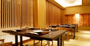 Un restaurant doté de portes coulissantes en bois, avec des tables dressées, où l’on trouve des assiettes, des verres et des menus.