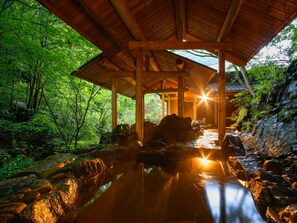Un pavillon en bois, avec un chemin de pierre menant à un élément décoratif aquatique, le tout entouré d’une végétation luxuriante.