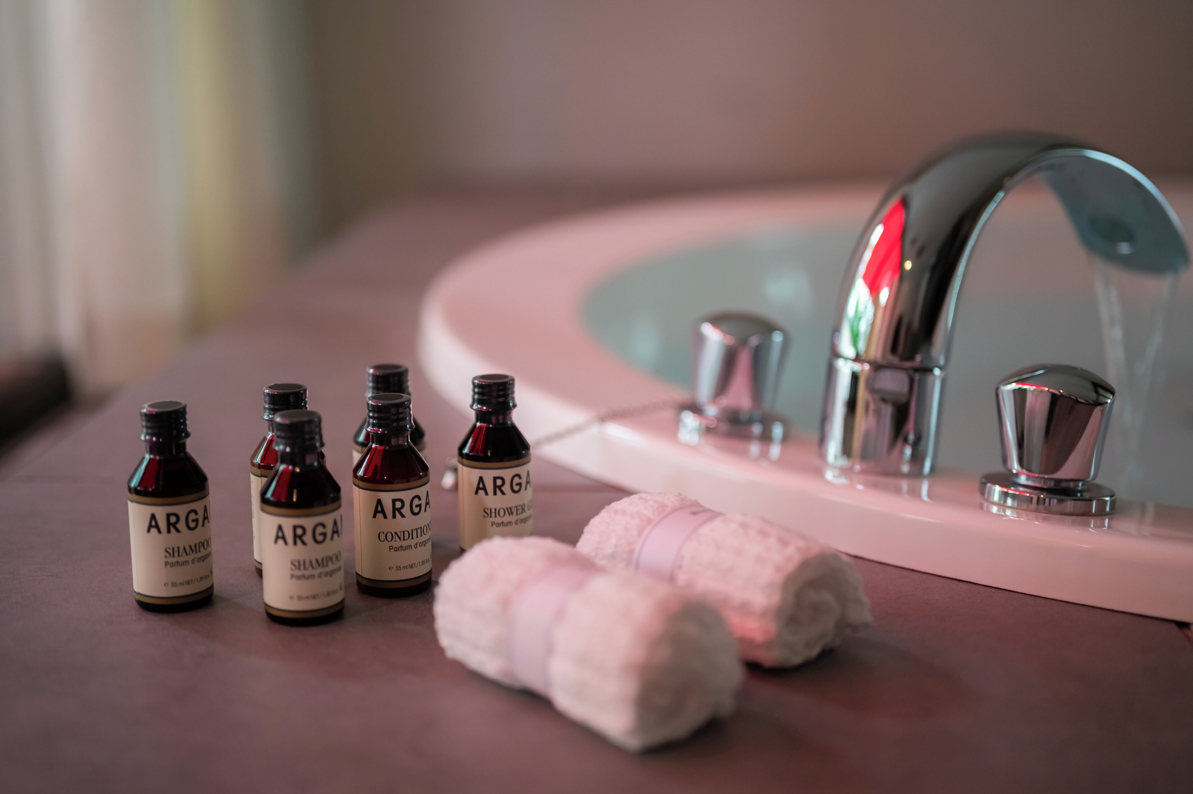 A bathroom sink with a mirror, a faucet, and four bottles of Arga shampoo and conditioner.