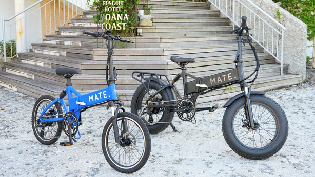 Dos bicicletas estacionadas en un sendero de grava frente a un edificio con un cartel que dice 'Resort Hotel Moana Coast'.