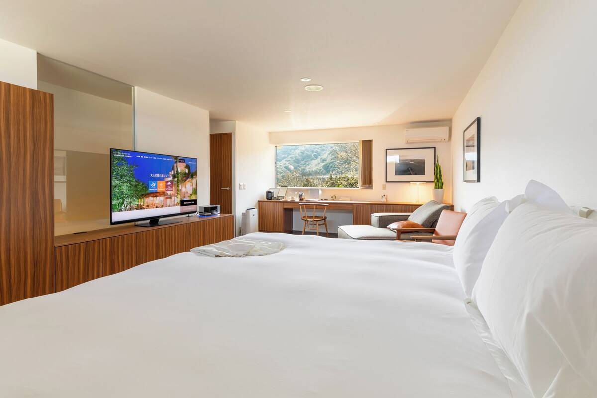 A modern hotel room with a large bed, a television, a desk, and a window with a view of the outdoors.