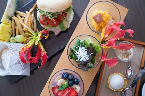 A meal with a sandwich, fries, a salad, and a fruit bowl on a wooden board. - Resort Hotel Moanacoast (Naruto)