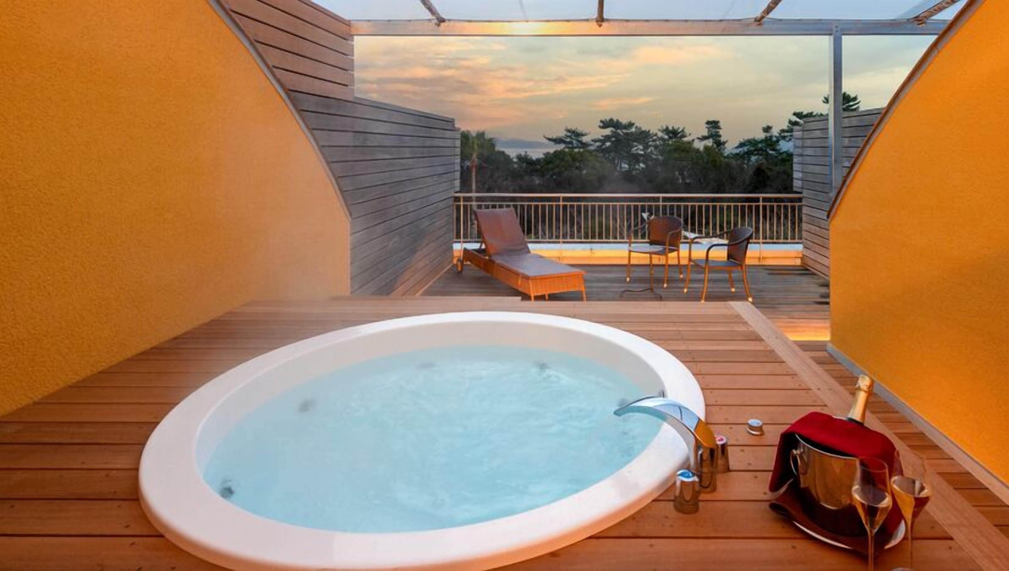 Un jacuzzi en una terraza de madera con vista a árboles y al atardecer.