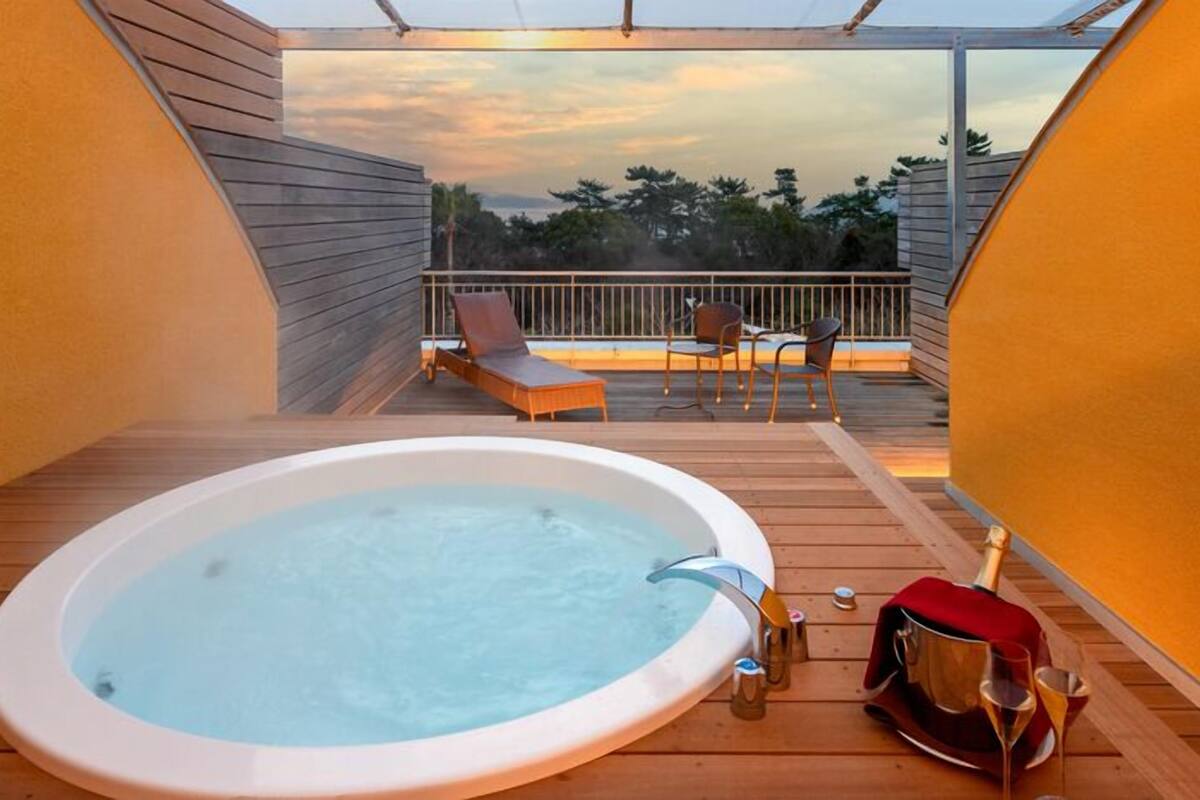 A hot tub on a wooden deck with a view of trees and a sunset.