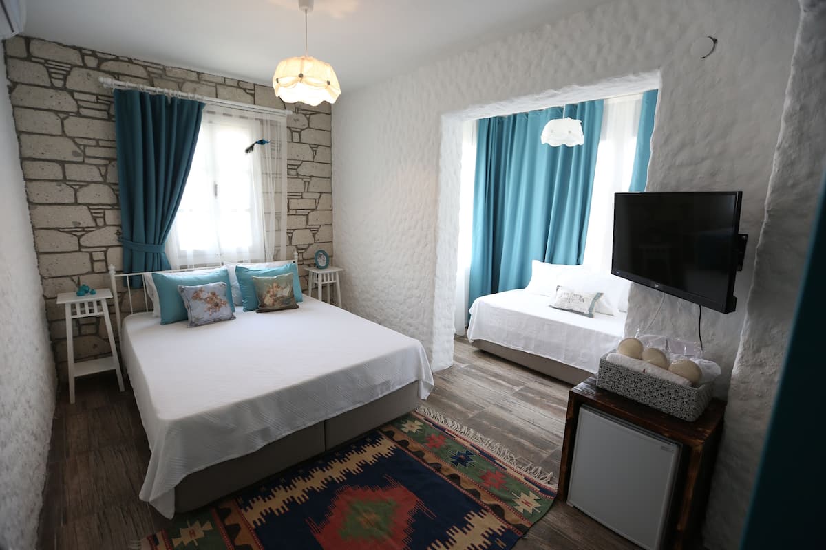 A bedroom with a large bed, a smaller bed, a TV mounted on the wall, a small table with a basket, and a patterned rug.
