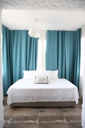 A bedroom with a large bed, teal curtains, white bedding, and a white pendant light.