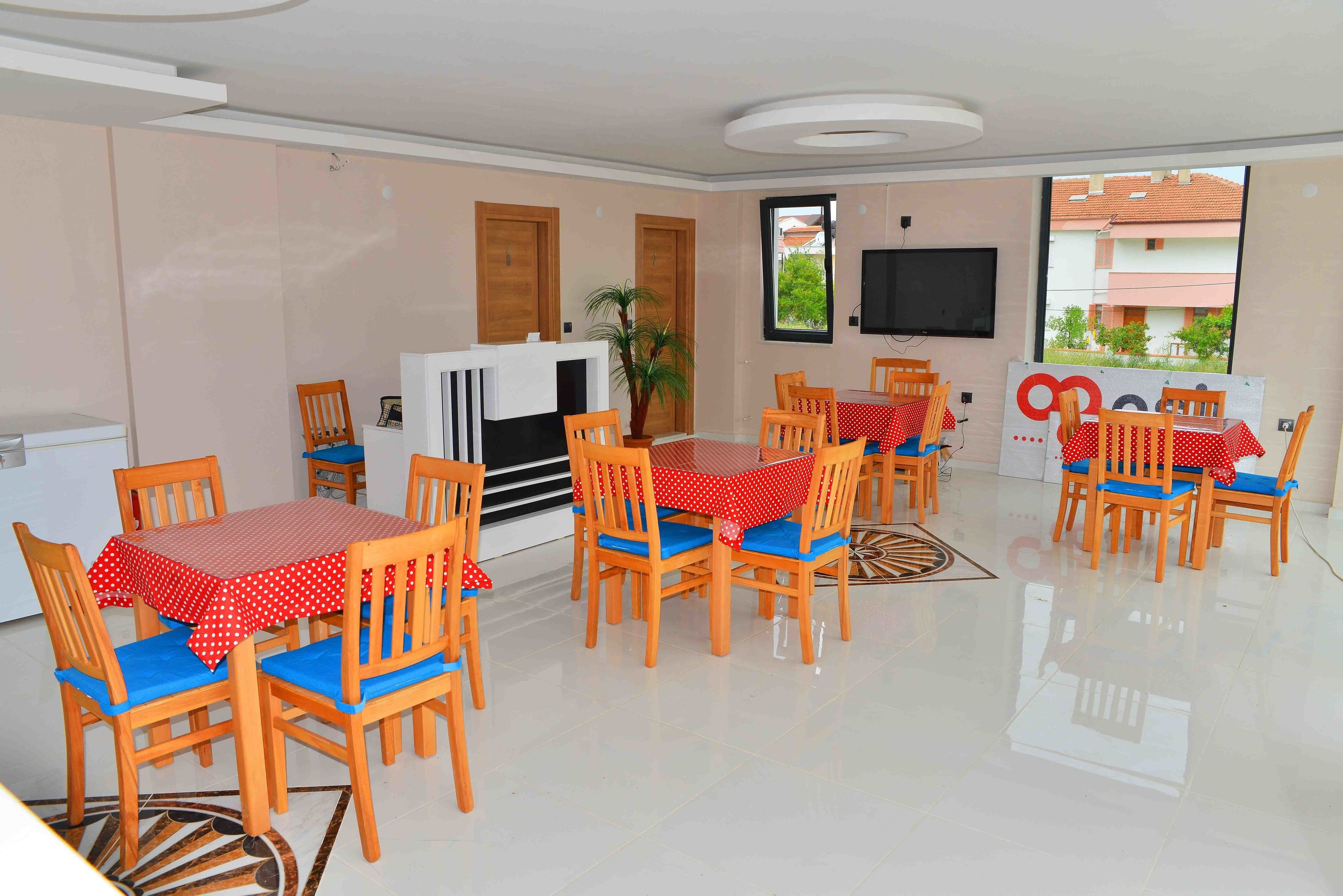 A dining area with wooden chairs and tables, a television, and a view of buildings outside.