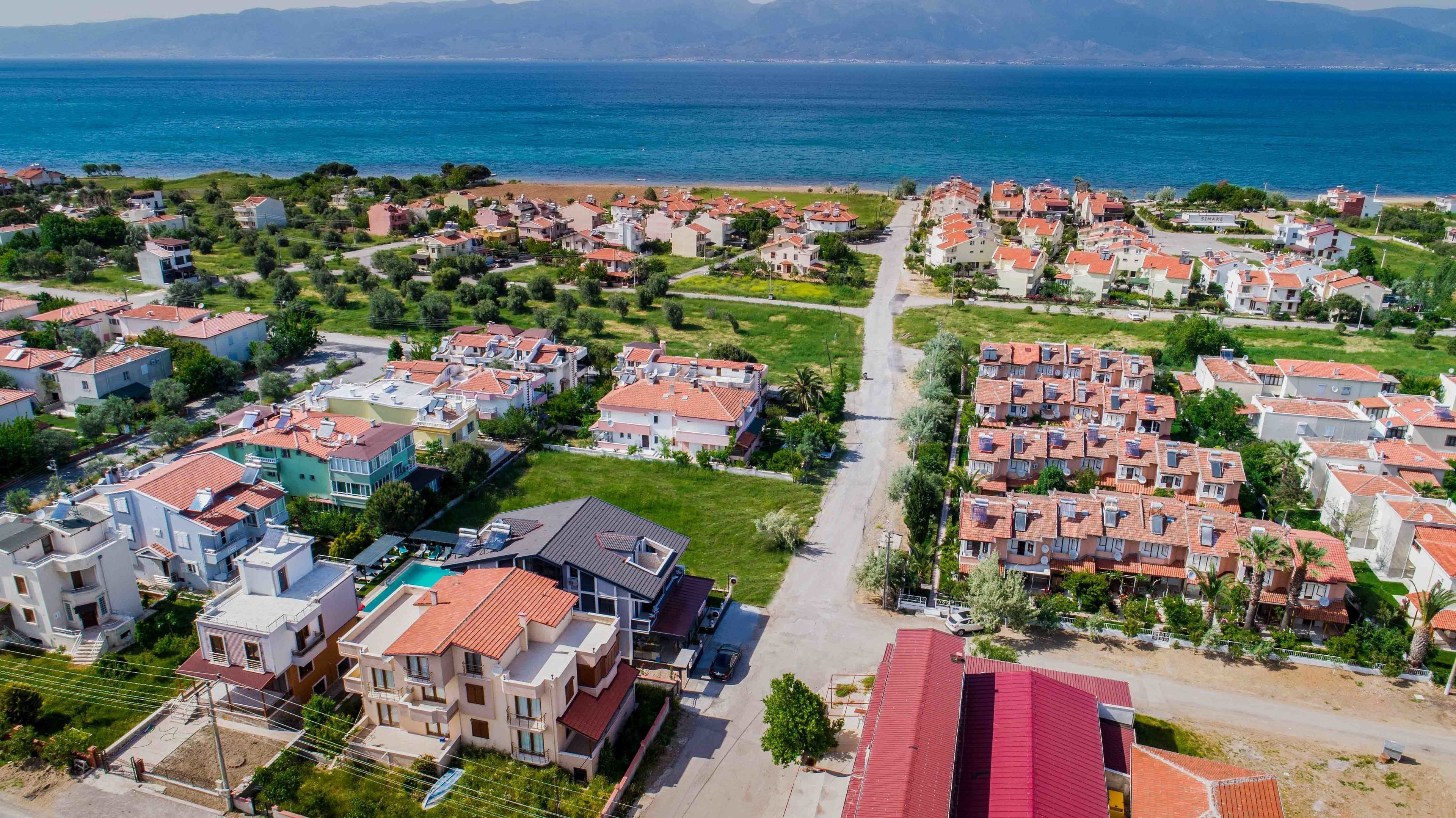 Zona residencial costera con casas modernas, una calle central y una playa al fondo.