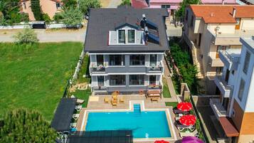 A two-story house with a swimming pool, outdoor furniture, and a garden.