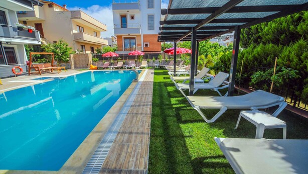 A swimming pool with lounge chairs and umbrellas, surrounded by a well-maintained lawn and buildings in the background. - Asil Apart Otel (Burhaniye)