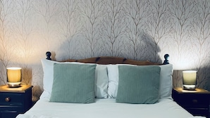A neatly made bed with white linens and green pillows, flanked by two bedside tables with lamps. - Ladybower Inn (Hope Valley)