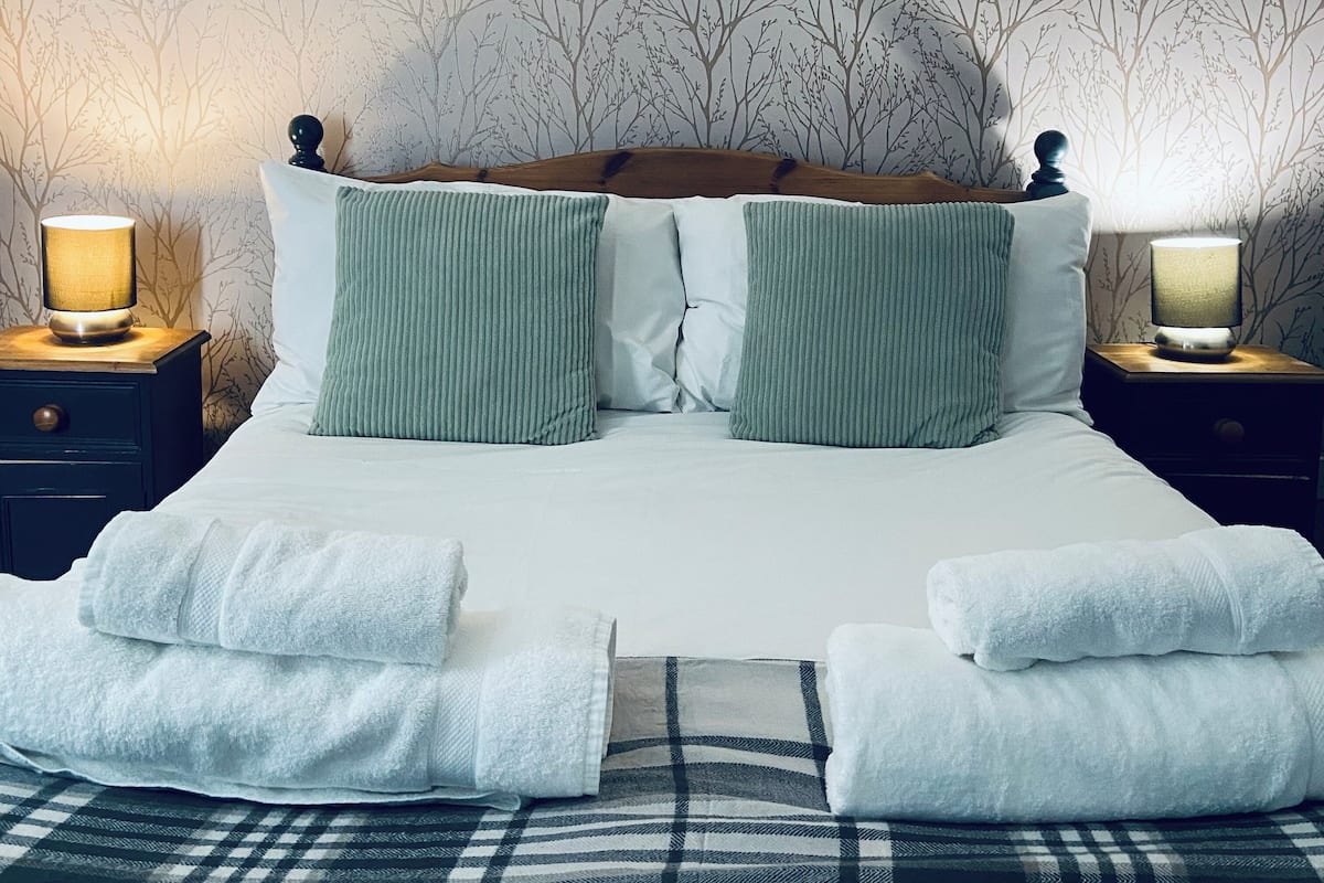 A neatly made bed with white linens and green pillows, flanked by two bedside tables with lamps.