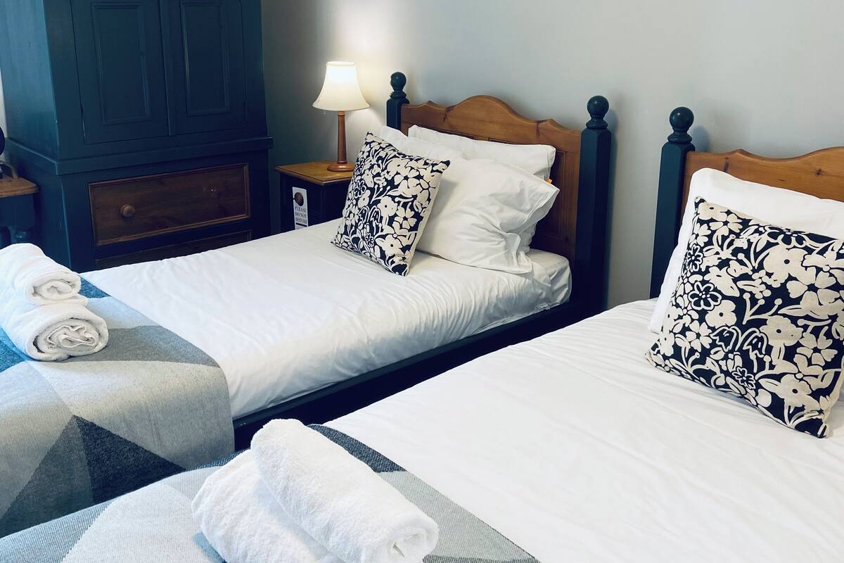 A hotel room with two beds, a wardrobe, a nightstand with a lamp, and towels on the beds.