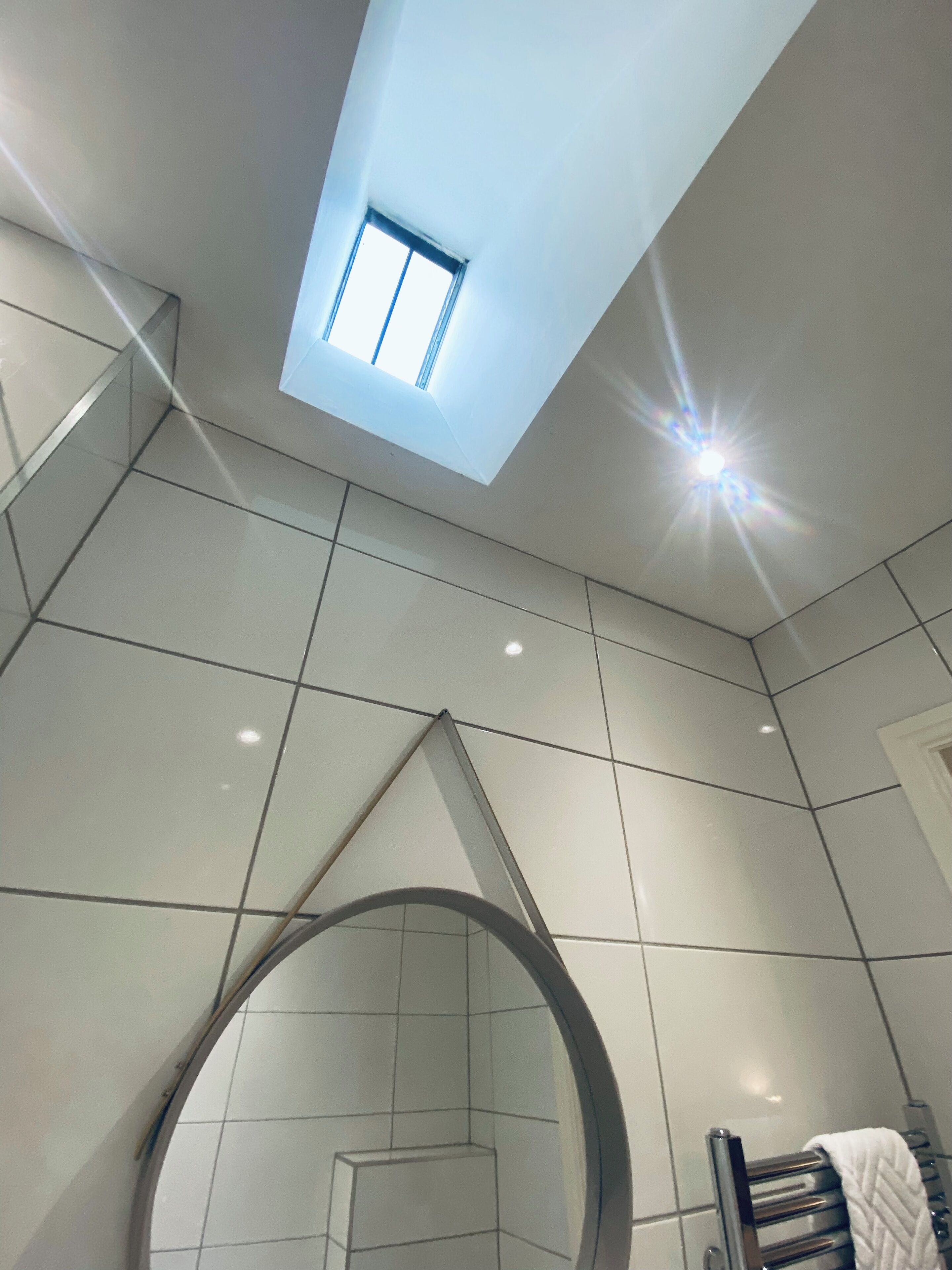 A modern bathroom with a skylight, tiled walls, and a circular mirror.