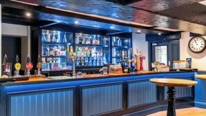 A bar with a blue counter, shelves of bottles, and a clock on the wall. - Ladybower Inn (Hope Valley)