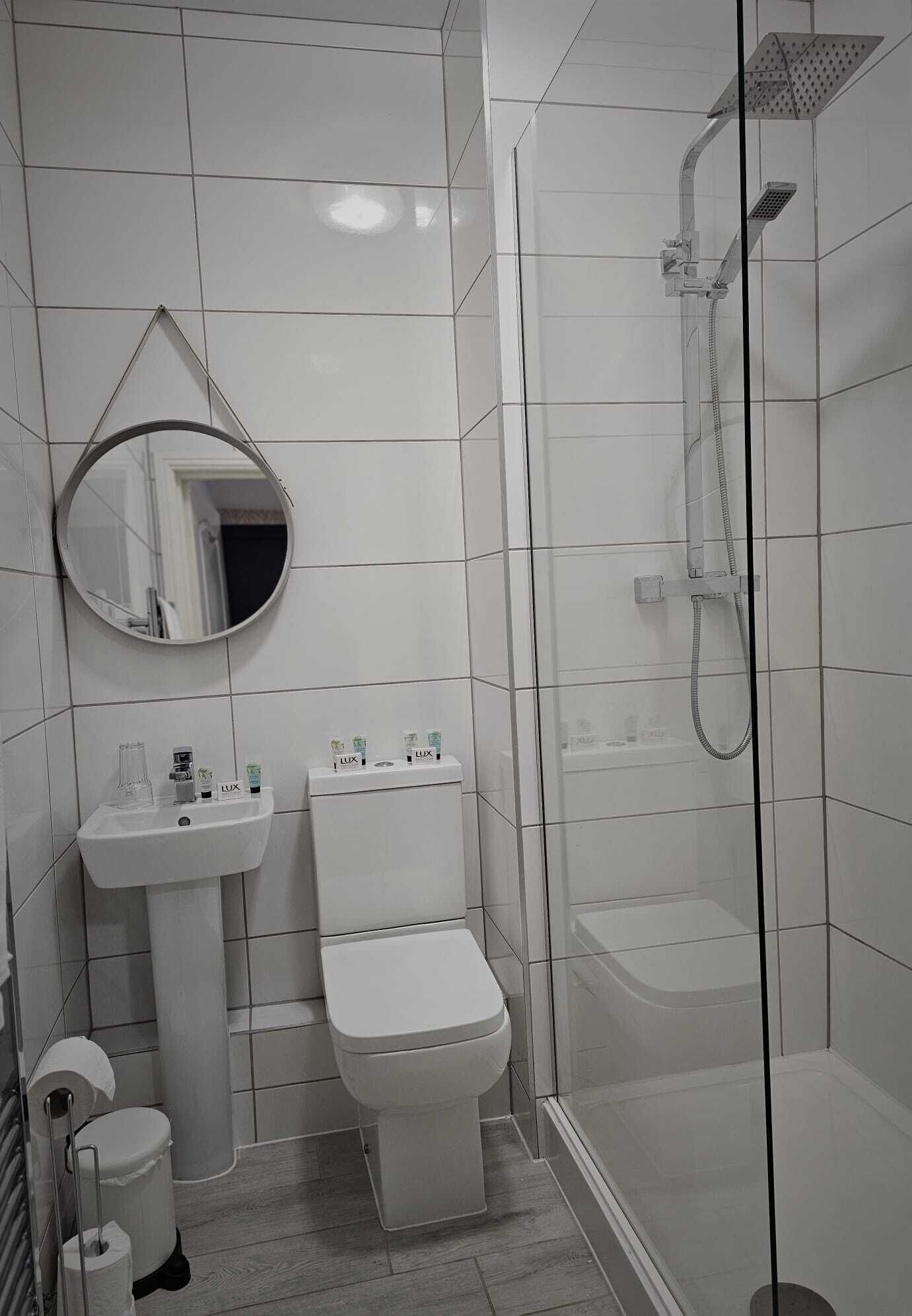 Un baño moderno con ducha de vidrio, lavamanos blanco y retrete.