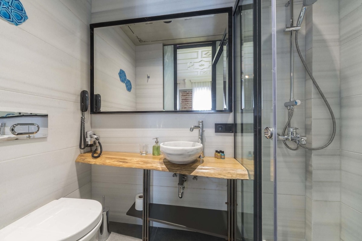 A modern bathroom with a glass shower enclosure, a white sink with a wooden countertop, and a toilet.