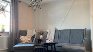 Una sala de estar moderna con un sofá gris, dos sillones, una pequeña mesa redonda y una lámpara colgante con forma de estrella.