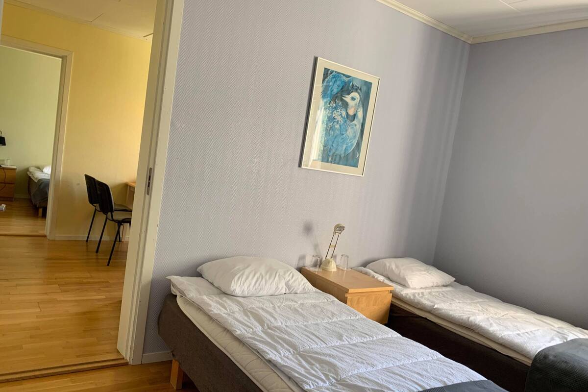Een kamer met twee eenpersoonsbedden, een houten nachtkastje, een ingelijst foto aan de muur en een stoel in de hoek.