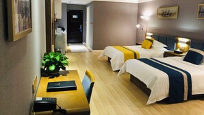 Habitación de hotel con dos camas, un escritorio con una computadora, una silla, una planta y una puerta que da a un pasillo.