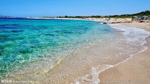 Una playa con agua turquesa cristalina, orilla de arena y algunas sombrillas.