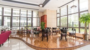 Un espacio interior amplio con ventanas grandes, suelo de madera y diversas disposiciones de asientos.
