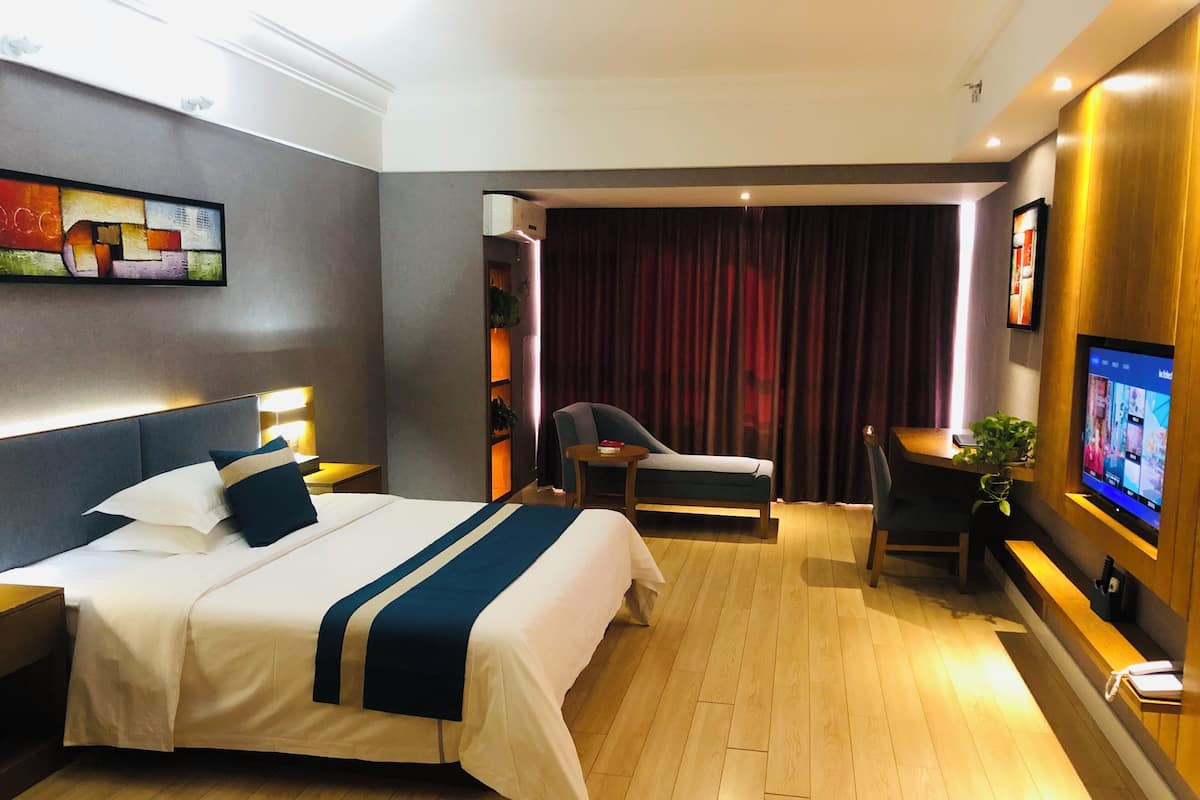 Habitación de hotel con una cama grande, un escritorio, una silla, un televisor y una cortina.