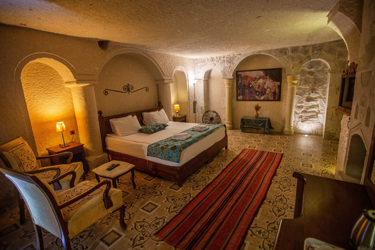 A room with a bed, a chair, a table, a lamp, and a fireplace.