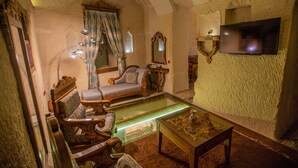 A room with a glass coffee table, a sofa, a chair, a television, and a mirror. - Hermes Cave Hotel (Nevsehir)