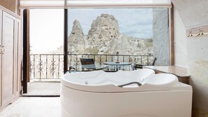 A modern bathroom with a large bathtub, a glass-enclosed balcony with a view of rock formations. - Hermes Cave Hotel (Nevsehir)