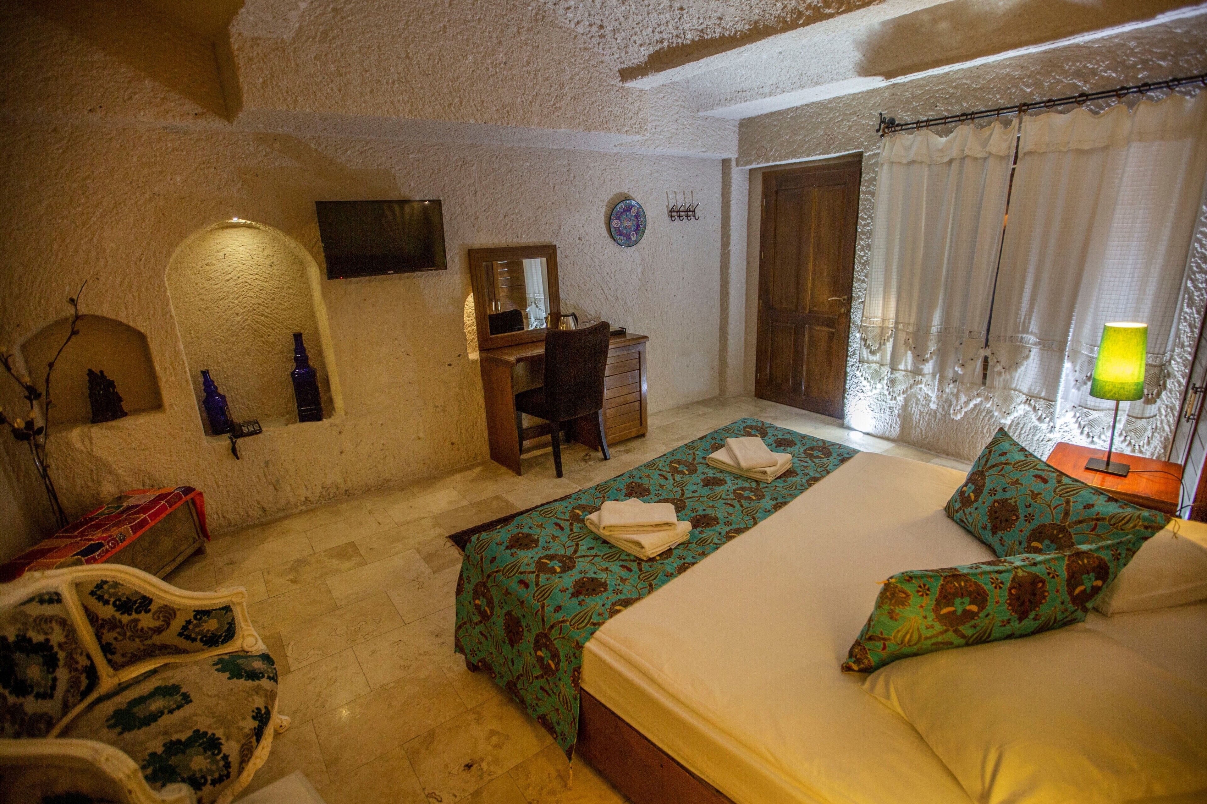 A bedroom with a bed, a desk, a chair, a TV, and a lamp.