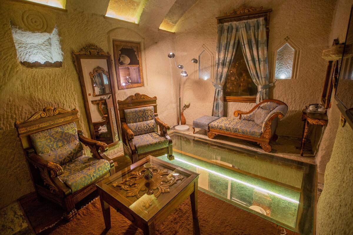 A room with antique furniture, including ornate chairs and a sofa, a glass table, and a decorative mirror.
