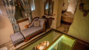 A room with a glass display case, a sofa, a bed, and a mirror on the wall. - Hermes Cave Hotel (Nevsehir)