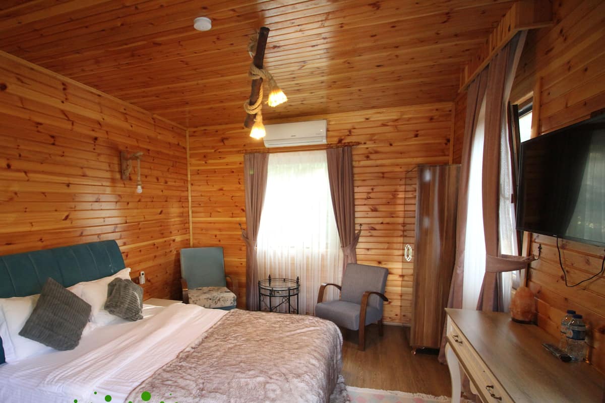 A wooden cabin bedroom with a bed, two chairs, a TV, and a small table.
