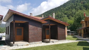 Deux bâtiments de style rustique, construits en rondins de bois, avec des fondations en pierre et des portes en bois, se dressent sur un fond de paysage montagneux.