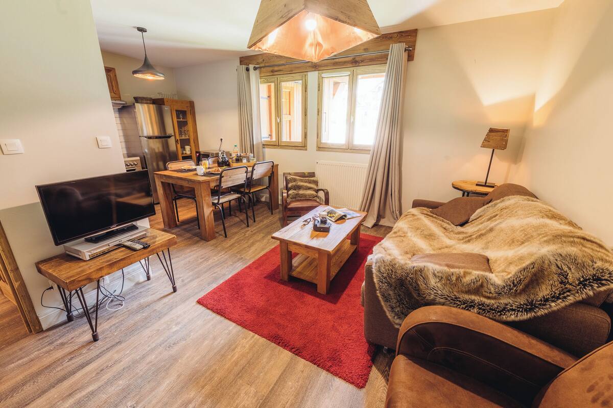 A cozy living room with a TV, wooden furniture, a red rug, and a sofa with a fur throw.