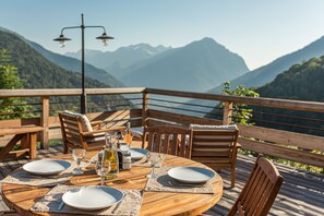 A wooden deck with a round table set for dining, overlooking a mountainous landscape. - Chalet La Perle d'Oisans (Vaujany)