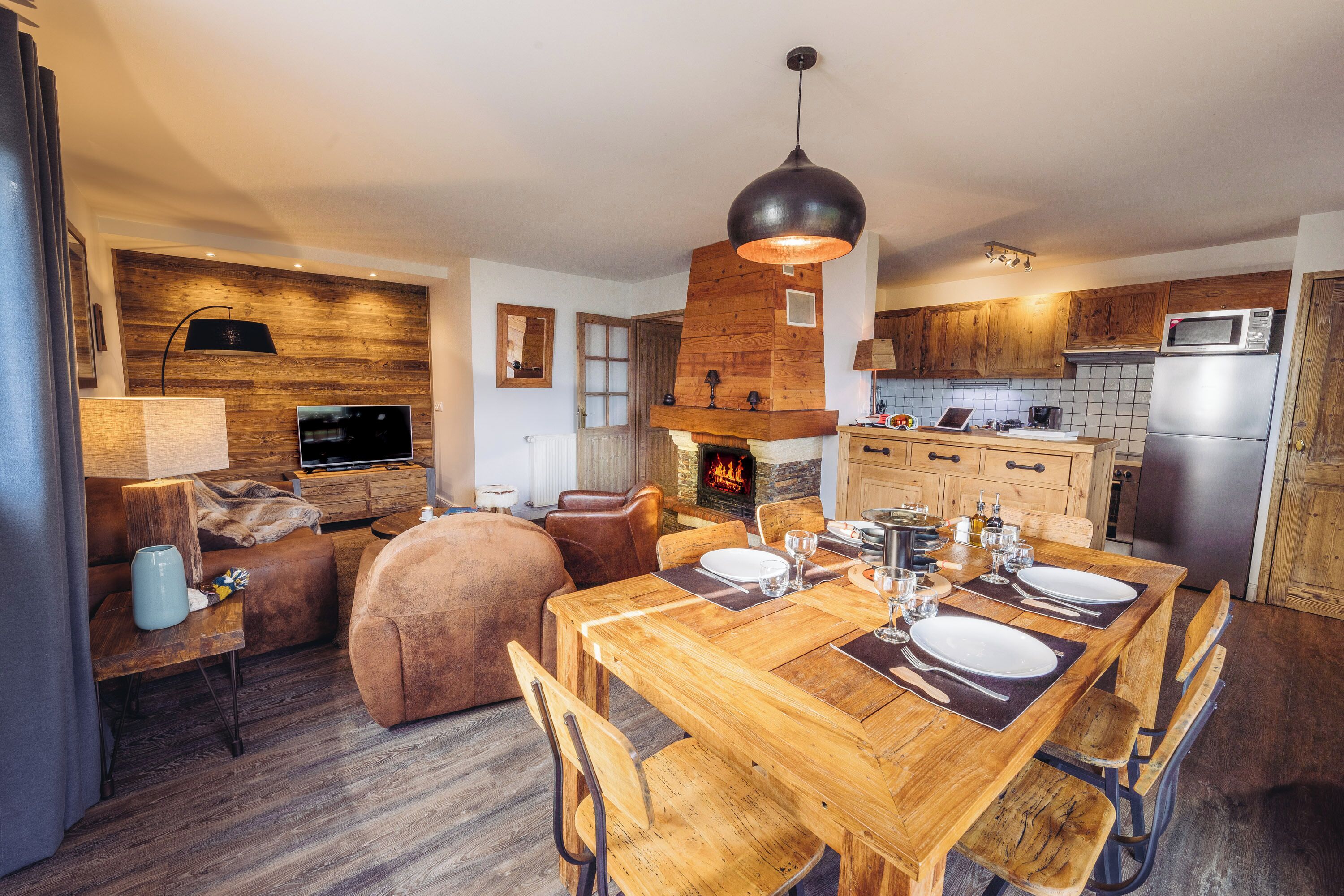 A modern kitchen with wooden cabinets, a dining table set for four, and a fireplace.